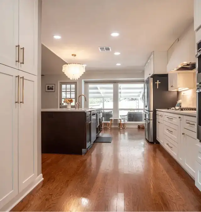 Kitchen with white cabinets, brass pulls, a dark island and wood floors running toward the living room