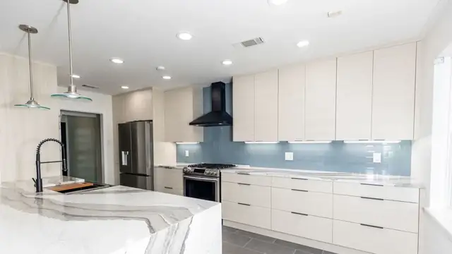 San Antonio kitchen remodel with flat-panel white cabinets, a veined quartz waterfall island, blue glass backsplash and black range hood