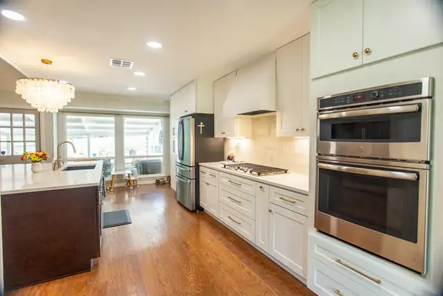 White kitchen with a dark wood island, crystal chandelier, double wall ovens and hardwood floors