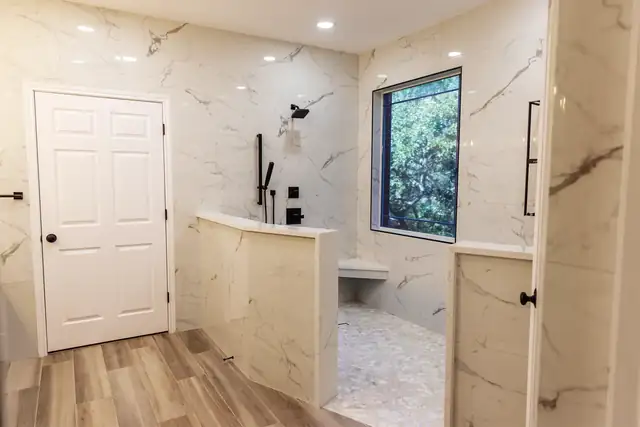 Marble-look walk-in shower with a low half wall, matte black fixtures and a window, remodeled by C&S