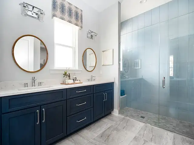 Navy double vanity with round mirrors next to a frosted glass walk-in shower in a C&S bathroom remodel
