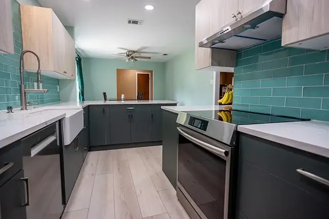 Kitchen remodel with a teal glass subway backsplash, dark lower cabinets, white quartz counters and farmhouse sink