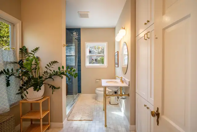 Bathroom remodel by C&S Remodeling with warm walls, a brass console sink, round mirror and a blue tile shower beyond